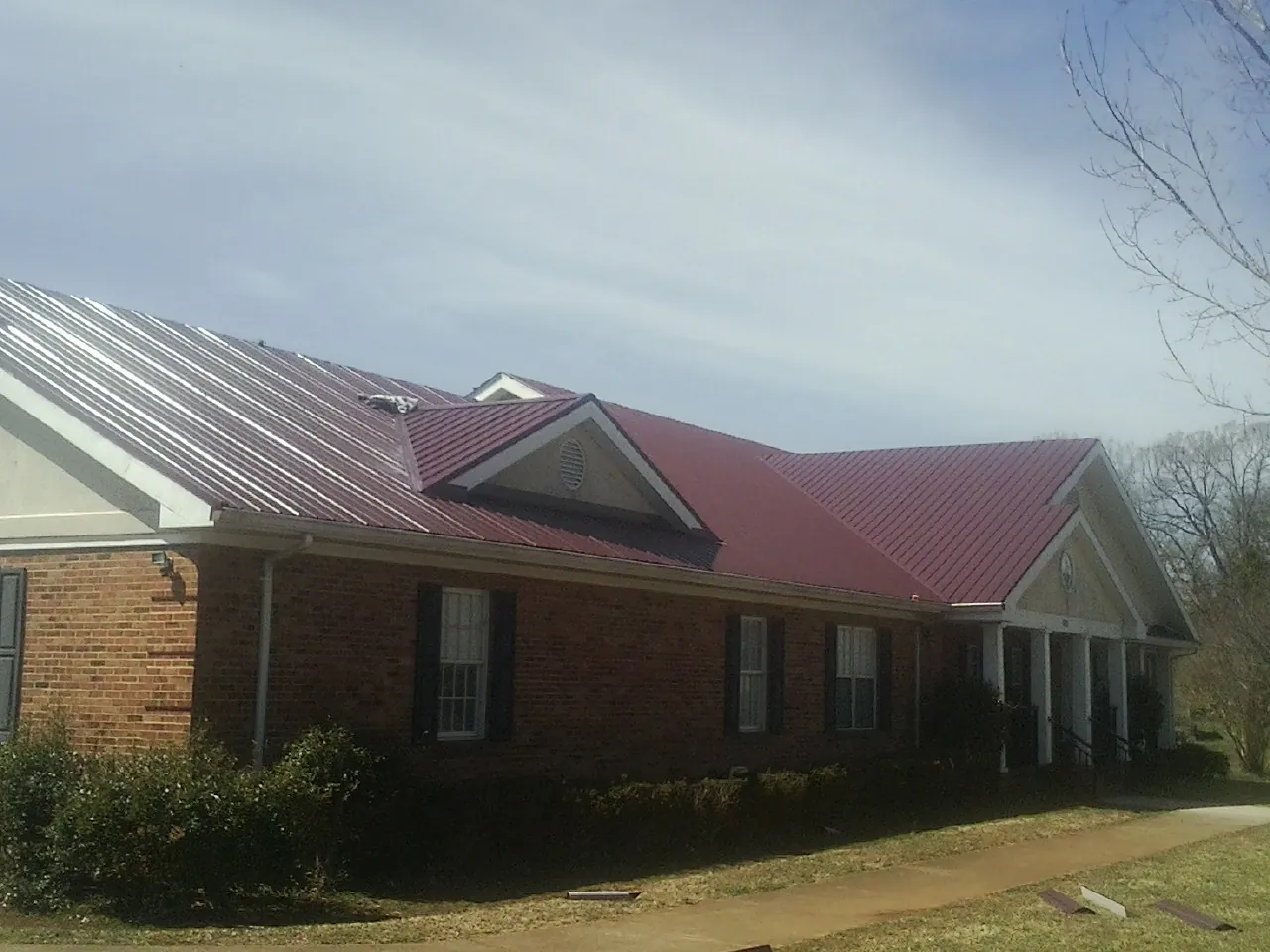 Red metal roof with gabled entries on a long brick building, from a Hail Damage Roof Repair job in Ilwaco