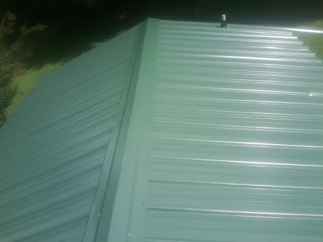 New green metal panels meeting at the ridge of a roof — Flat Roof Repair work by our crew in Ilwaco