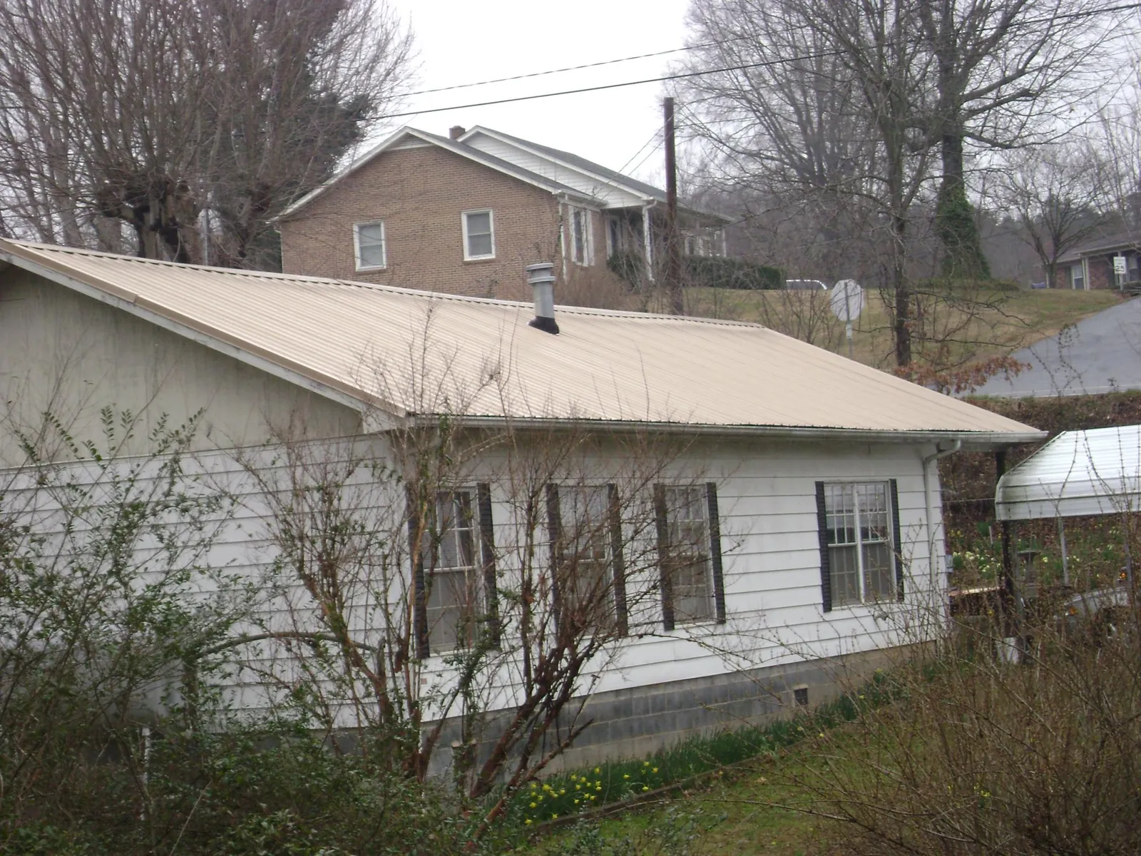 Tan metal roof on a white sided house set into a hillside — Commercial Roofing by Roofing Brothers in Ilwaco